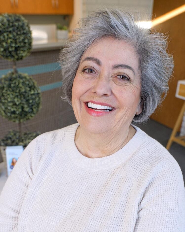 Female patient smiling after receiving full-arch dental implant restoration